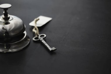 Otel resepsiyonunda parlak gümüş bir metal zil. Otel odasındaki masada bir zil ve kapı anahtarıyla birlikte bir masa. Anahtar ve zil bir otelde..
