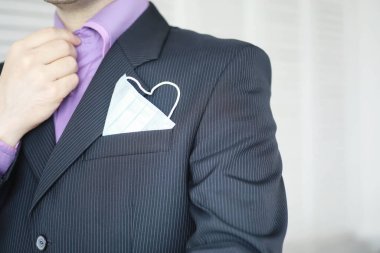 Tek kullanımlık bir tıbbi maske peçeteden sarkıyor. Takım elbiseli ve kot pantolonlu tek kullanımlık maskeli bir adam. Bireysel solunum koruması.