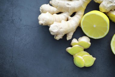 Zencefil kökü bütün ve dilimlenmiş. Koyu arkaplanda limonlu zencefil çayı. Taş zeminde taze zencefil kökü. Vitaminler. Üst Manzara. Metnin için boş yer.