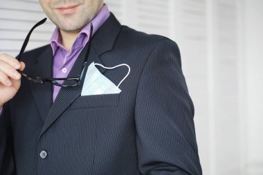 Tek kullanımlık bir tıbbi maske peçeteden sarkıyor. Takım elbiseli ve kot pantolonlu tek kullanımlık maskeli bir adam. Bireysel solunum koruması.