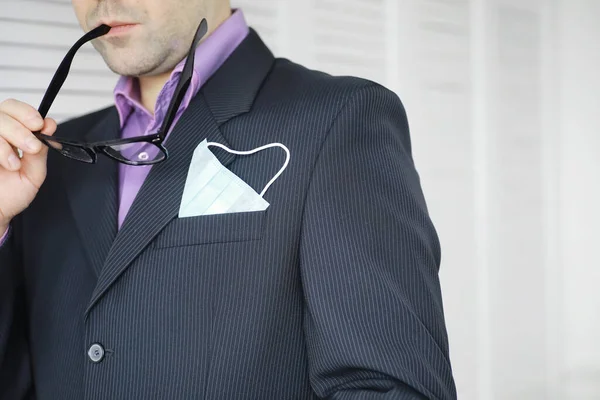 Tek kullanımlık bir tıbbi maske peçeteden sarkıyor. Takım elbiseli ve kot pantolonlu tek kullanımlık maskeli bir adam. Bireysel solunum koruması.