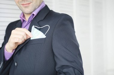 Tek kullanımlık bir tıbbi maske peçeteden sarkıyor. Takım elbiseli ve kot pantolonlu tek kullanımlık maskeli bir adam. Bireysel solunum koruması.