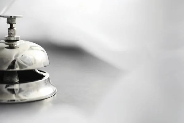 A shiny silver metal bell at hotel reception. A table in the hotel at the concierge with a bell and a door key. Key and bell in a hotel.