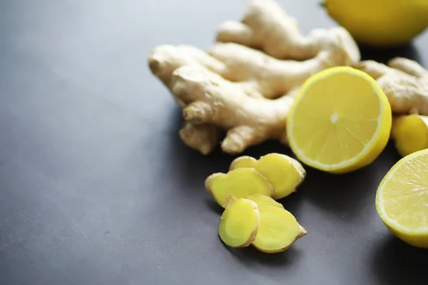 Ginger root whole and sliced. Ginger tea with lemon on the dark background. Fresh ginger root on stone background. Vitamins. Top view. Free space for your text.