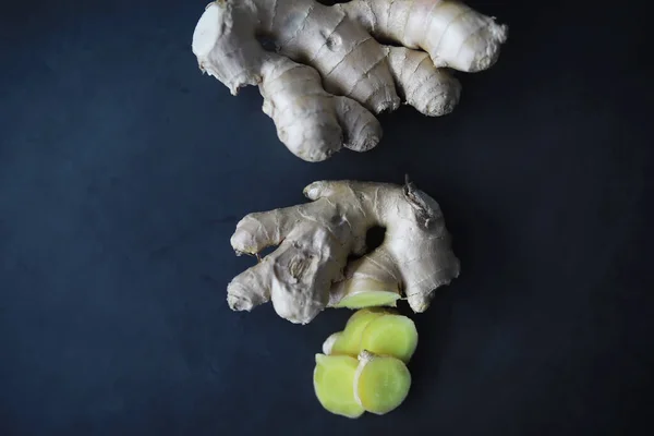 Ginger root whole and sliced. Ginger tea with lemon on the dark background. Fresh ginger root on stone background. Vitamins. Top view. Free space for your text.