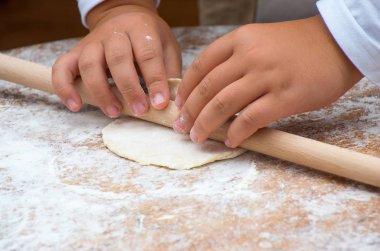 Ahşap masa üzerinde oklava ile çalışırken hamur çocuk eller