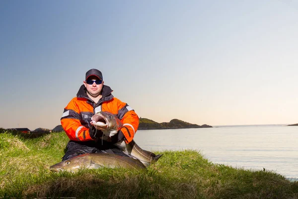 Fischer sitzt mit einem riesigen Fisch in der Hand am Ufer. e — Stockfoto