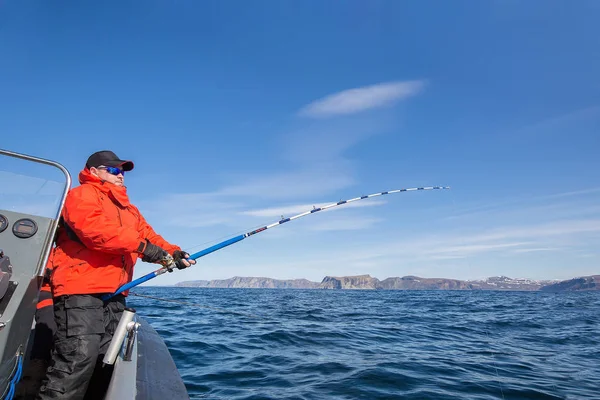 Mann zieht einen Fisch aus dem Wasser. rote Jacke. Sportbrille. fische — Stockfoto