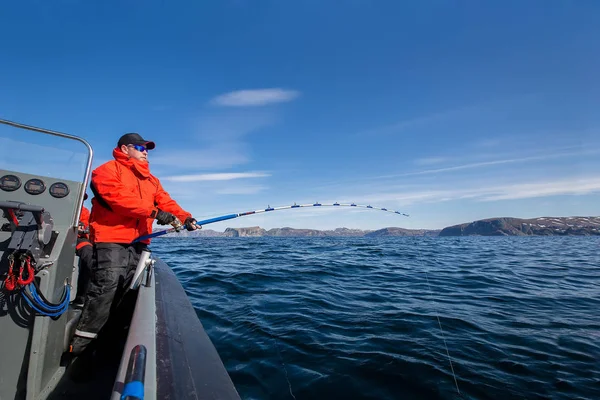 Mann zieht Fisch aus dem Meer. Angelrute biegt sich. rote Jacke. Freizeit — Stockfoto