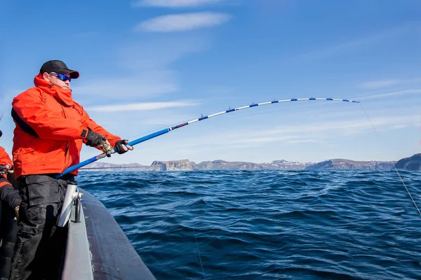 Mann zieht Fisch aus dem Meer. Spinnbiegung. rote Jacke. Sport gla — Stockfoto