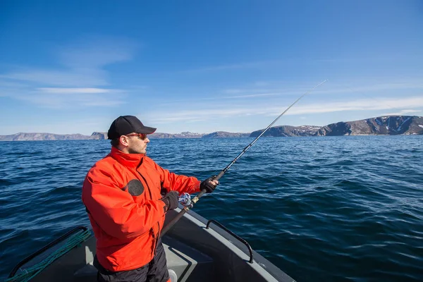 Fischer Athlet mit Angelrute in der Hand. ein Boot. Wasser. — Stockfoto