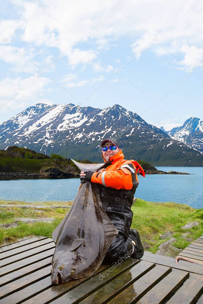 Man fisherman with huge fish Halibut. Behind the beautiful lands