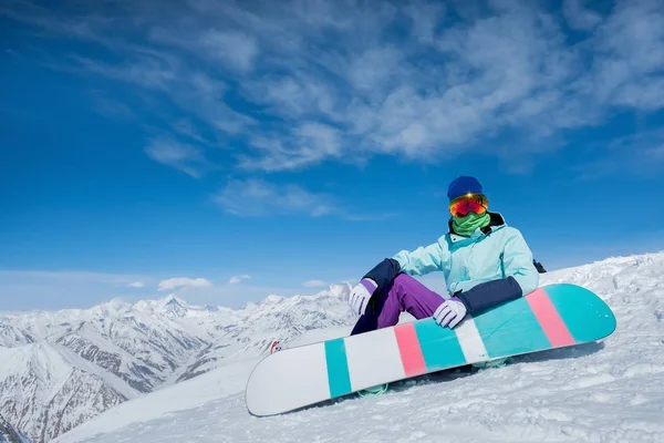 Κοπέλα κάθεται πάνω στο χιόνι με ένα Διοικητικό Συμβούλιο snowboard. Το χειμώνα. Το — Φωτογραφία Αρχείου