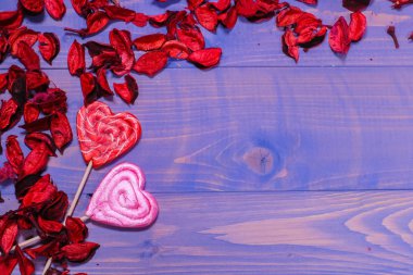 İki kalp şeklindeki lolipop kırmızı çiçek yapraklarında yatıyor. Mavi arka plan, ağaç. Sevgililer günü konsepti, yıldönümü, düğün. Yazıtlar için alanı kopyala.