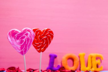 İki kalp şeklinde lolipop. Kırmızı ve pembe kalpler. Keçeli kumaştan gelen çok renkli harflerle yazılmış bir aşk. Kırmızı Kalpler Sevgililer Günü aşk konsepti. Yazıtlar için alanı kopyala