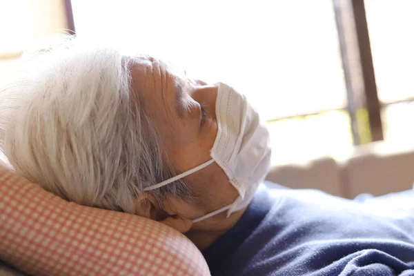 Seniorin Liegt Mit Operationsmaske Zum Virenschutz Auf Dem Pflegebett — Stockfoto