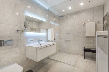 Geniş ışıklandırmalı ayna, lavabo ve cam duşlu güzel modern banyo.