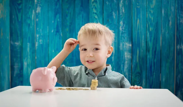 Hároméves gyermek ül az asztalnál pénzérmékkel és nagy bank — Stock Fotó