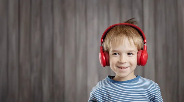 Mały chłopiec na drewnianym tle z czerwonymi słuchawkami — Zdjęcie stockowe