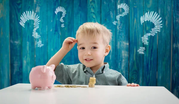 Niño de tres años sentado st la mesa con monedas de dinero y biggybank —  Fotos de Stock