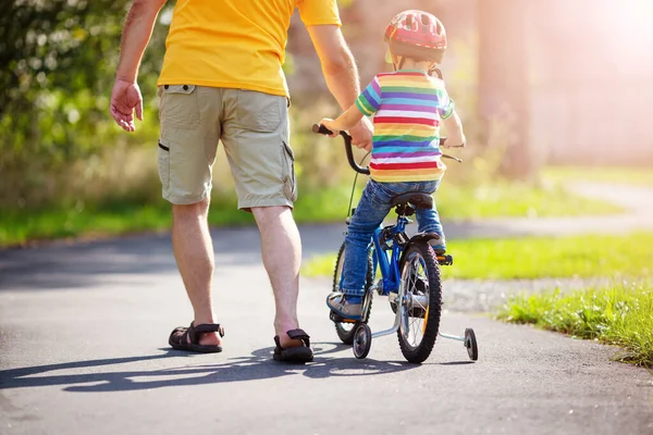 Un niño en bicicleta en casco con padre en camino de asfalto — Foto de Stock