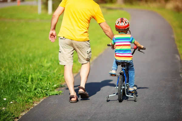 Un niño en bicicleta en casco con padre en camino de asfalto — Foto de Stock