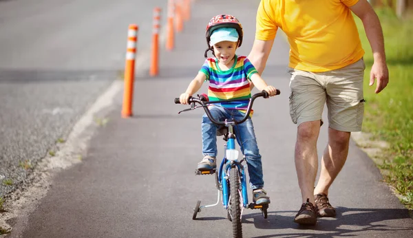 Een kind op een fiets in helm met vader op asfaltweg — Stockfoto