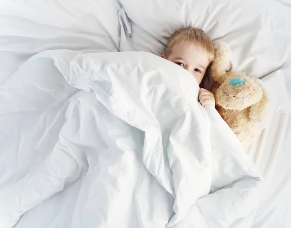 Niño somnoliento acostado en la cama con ropa de cama blanca —  Fotos de Stock