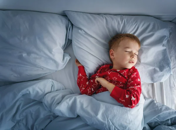 Schläfriger Junge, der mit blauer Bettwäsche im Bett liegt. Müdes Kind im Schlafzimmer — Stockfoto