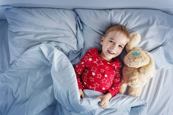 Niño somnoliento acostado en la cama con ropa de cama blanca —  Fotos de Stock