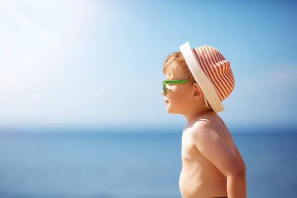 Маленький мальчик улыбается на пляже в шляпе в солнечных очках — стоковое фото