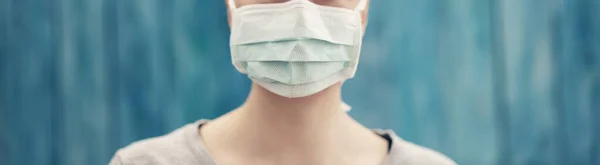 Junge Frau in medizinischer Gesichtsschutzmaske drinnen auf blauem Hintergrund — Stockfoto