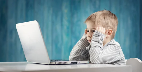 Glad fem år gammal barn sitter med en bärbar dator vid bordet — Stockfoto
