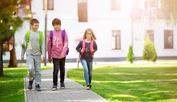 Niños con mochilas de pie en el parque cerca de la escuela — Foto de Stock