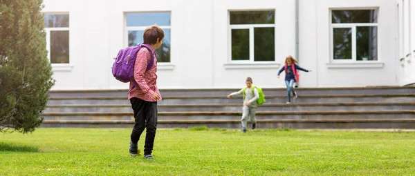 Bambini con zaini in piedi nel parco vicino alla scuola — Foto Stock