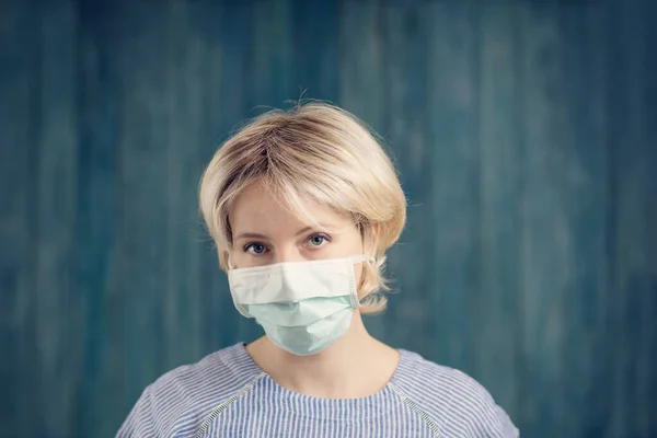 Jeune femme en masque médical de protection du visage à l'intérieur sur fond bleu — Photo