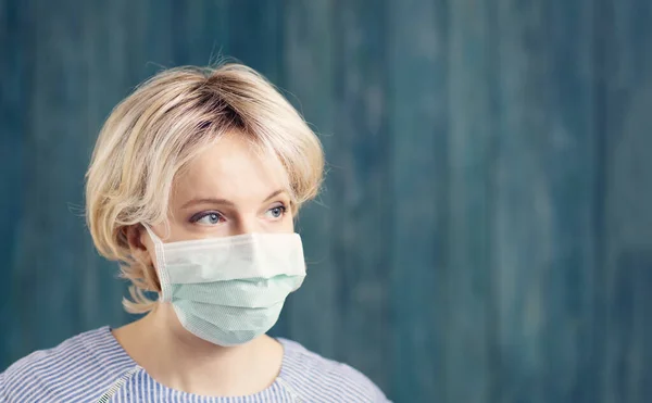 Молода жінка в медичній масці для захисту обличчя в приміщенні на синьому фоні — стокове фото