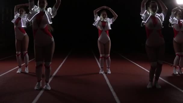 Cheerleaders equipe se movendo sincronicamente em trajes luminosos — Vídeo de Stock