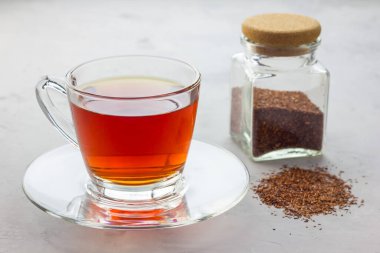 Bir fincan sağlıklı bitki çayı, cam bardakta kırmızı çay ve arka planda kuru çay.