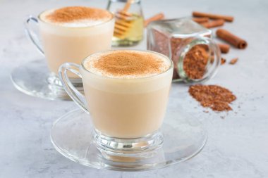 Tarçınlı, cam bardakta ve arka planda yatay malzemelerle kaplanmış sağlıklı robolar kırmızı latte.