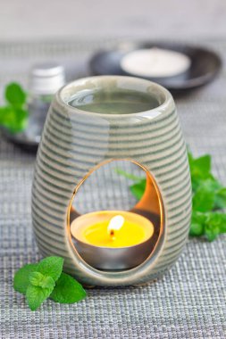 Aroma lambasındaki nane yağı gri hasırda, kaplıca arka planında, dikey