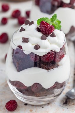 Browni, krem peynirli krema ve ahududu bardakta, dikey.