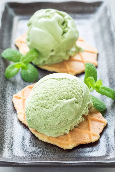 Matcha green tea ice cream balls served with waffles on black plate, vertical