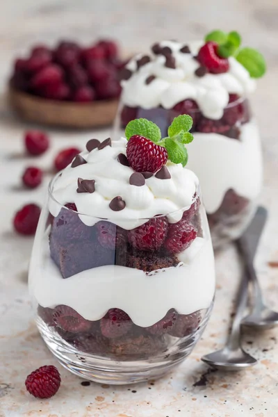 Browni, krem peynirli krema ve ahududu bardakta, dikey.