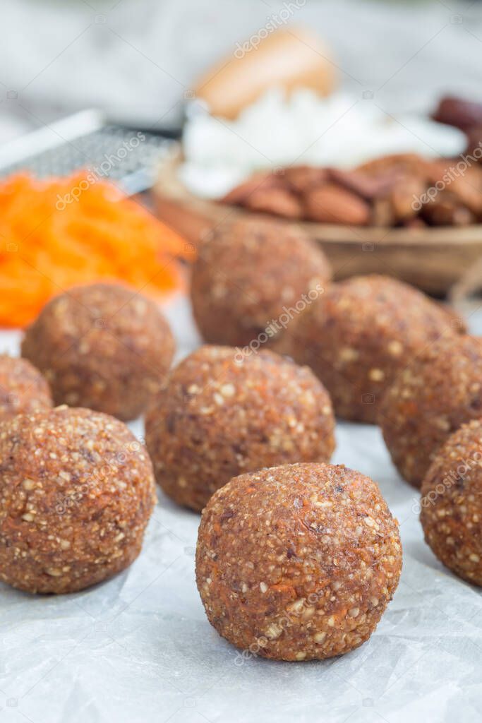 Healthy paleo energy balls with carrot, nuts, dates and coconut flakes, on parchment, vertical