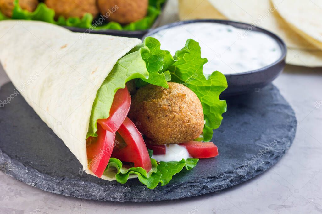 Chickpea falafel balls with vegetables and white sauce, roll sandwich preparation, horizontal, copy space