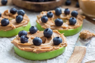 Sağlıklı sandviç. Fıstık ezmeli ve yaban mersinli yeşil elma mermileri ahşap masada, yatay.
