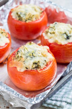 Kinoayla doldurulmuş fırınlanmış domatesler ve eritilmiş peynirle kaplı ıspanak fırın kabında, dikey ve yakın çekim