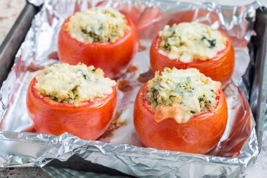 Kinoa ile doldurulmuş fırında domates ve eritilmiş peynirle kaplı ıspanak fırın kabında, yatay ve yakın plan.