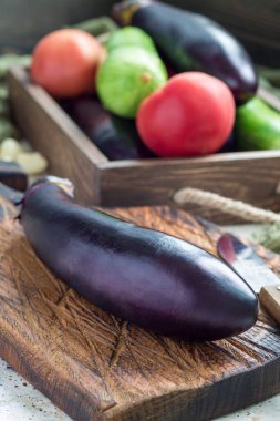 Sebze yemeği hazırlıyorum. Tahta kesme tahtasında patlıcan, arka planda sebzeler, dikey